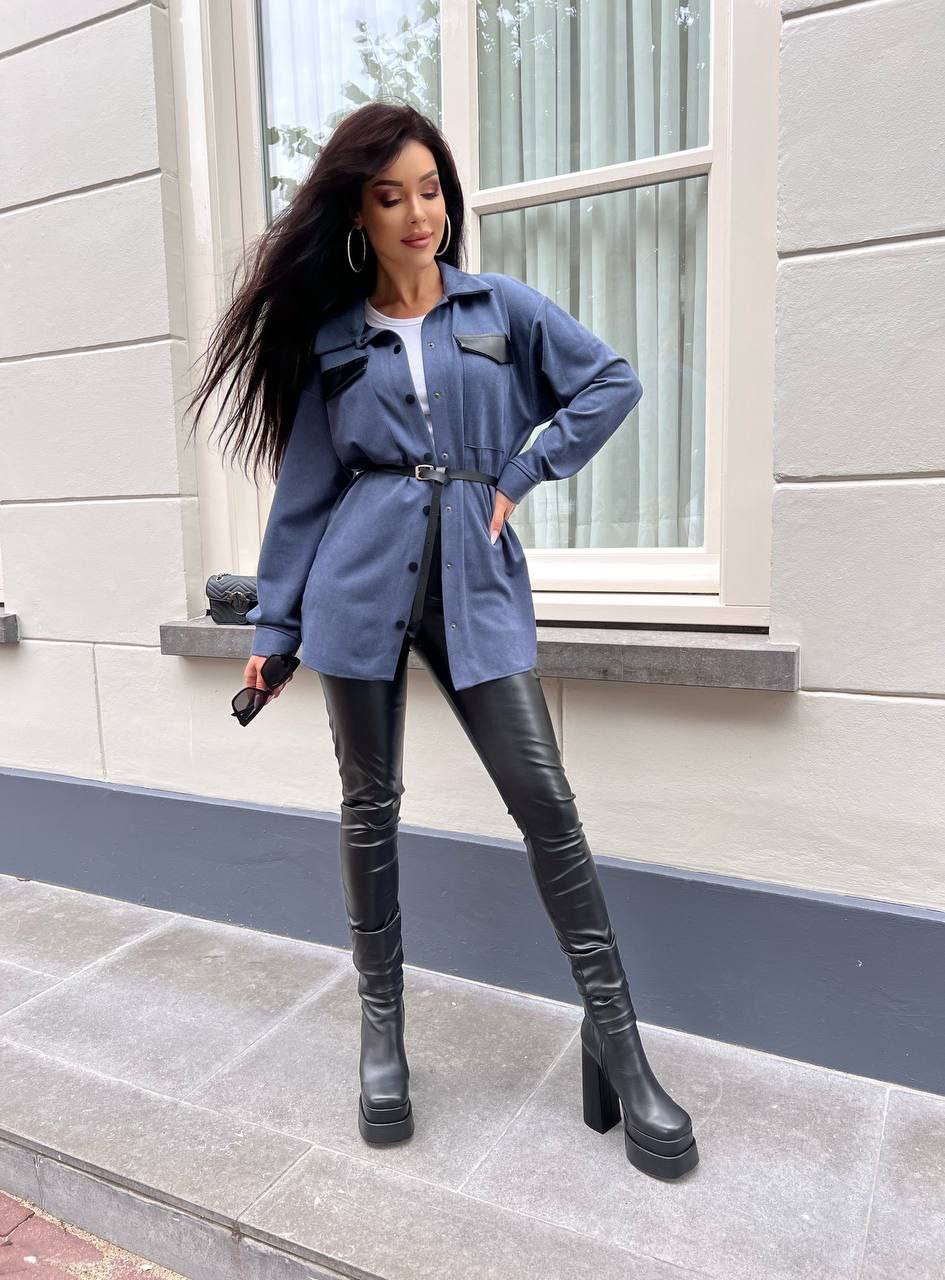 Woman in blue jacket and black leather pants standing on a sidewalk.