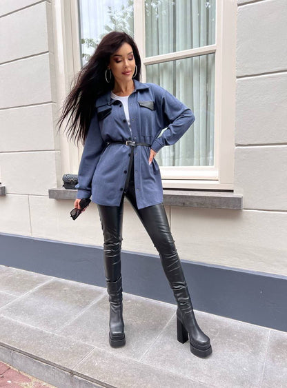 Woman in blue jacket and black leather pants standing on a sidewalk.