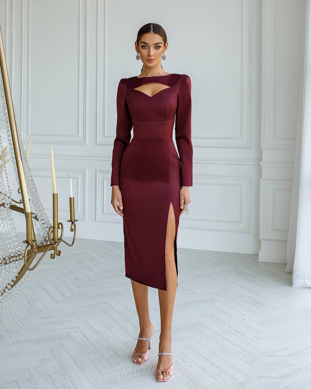 Woman wearing a burgundy dress with a high slit in a room with white walls and a chandelier.