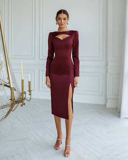 Woman wearing a burgundy dress with a high slit in a room with white walls and a chandelier.