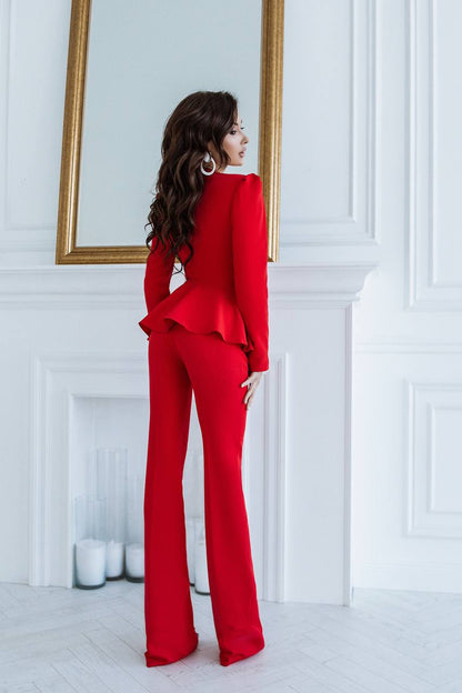Woman in a red outfit standing in a room with white walls and a gold-framed mirror.