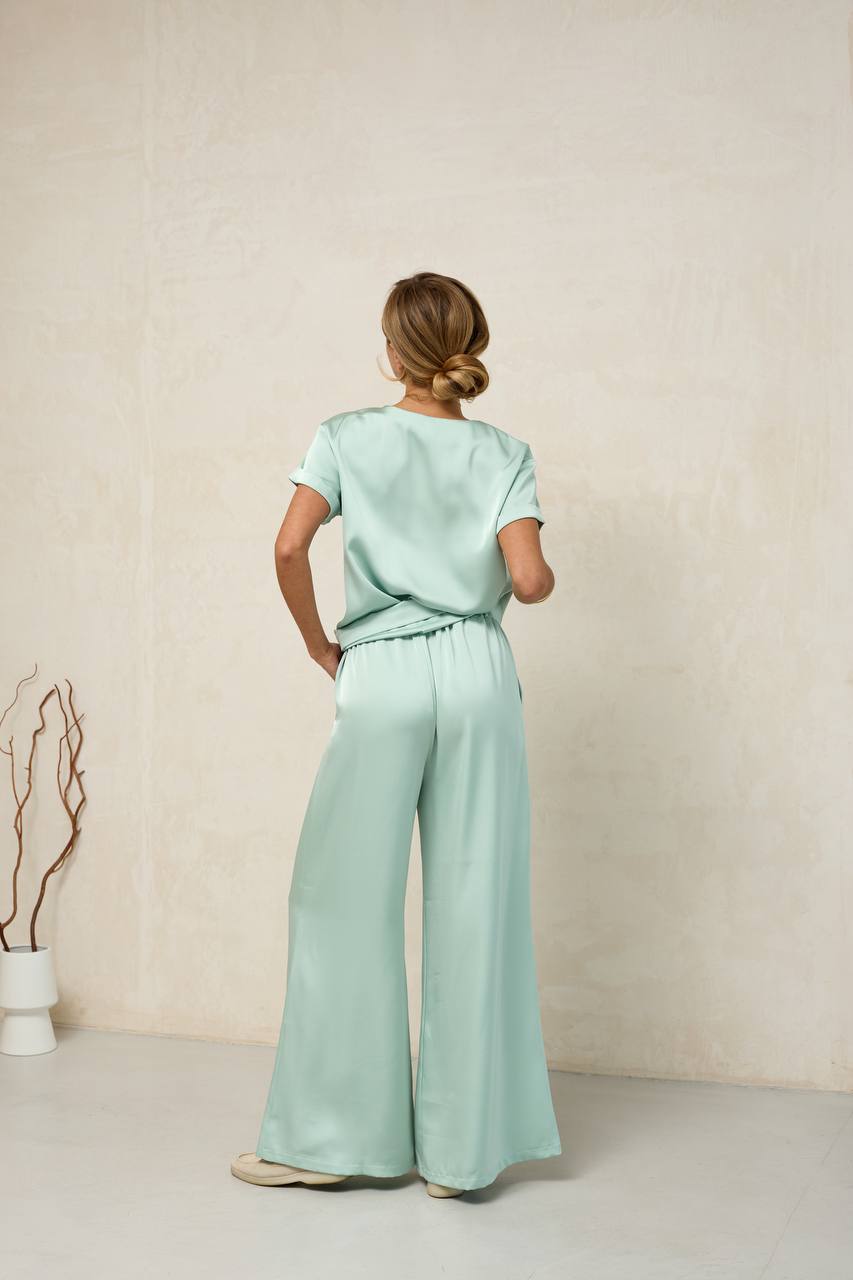 Person wearing a light green outfit standing against a plain background