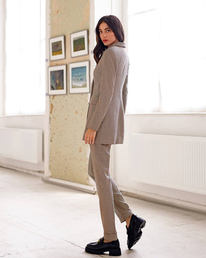 Woman in a gray checkered suit standing in a bright room with large windows.