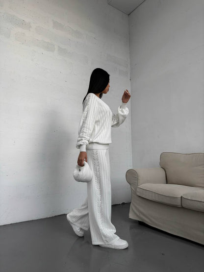 Person in a white outfit standing in a minimalistic room with a beige sofa.