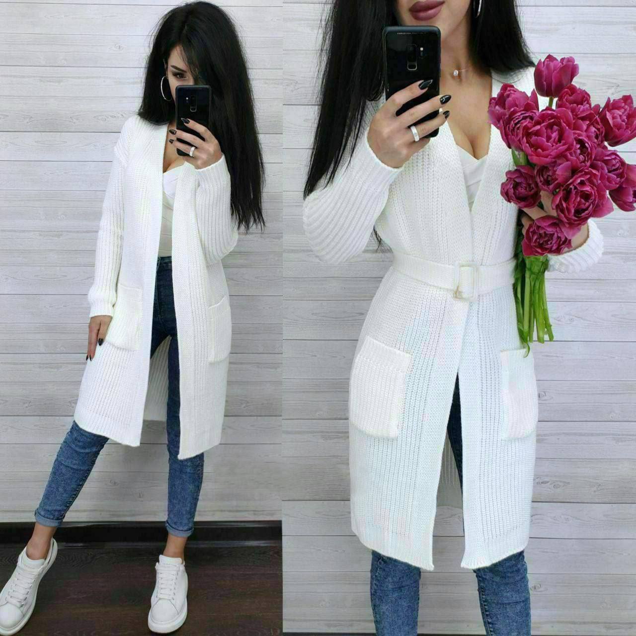 Woman wearing a white long cardigan, blue jeans, and white sneakers, holding pink tulips.