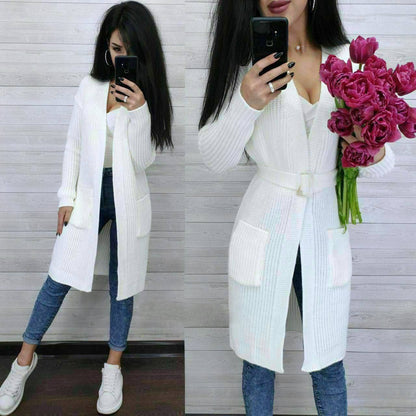 Woman wearing a white long cardigan, blue jeans, and white sneakers, holding pink tulips.
