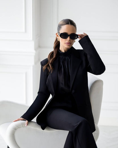 Woman in a black outfit sitting on a white chair with a white background