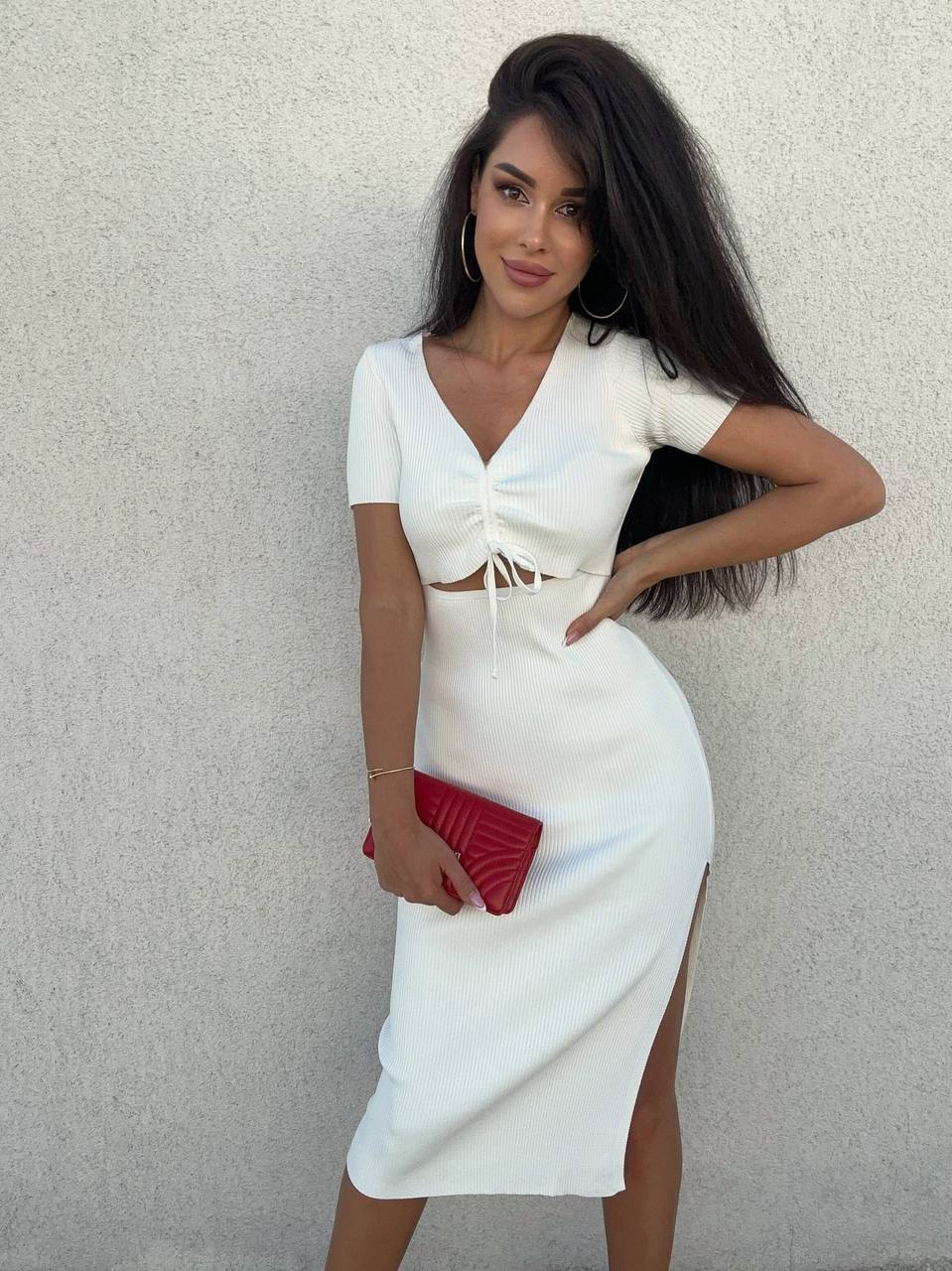 Woman in a white dress with a red clutch against a plain background