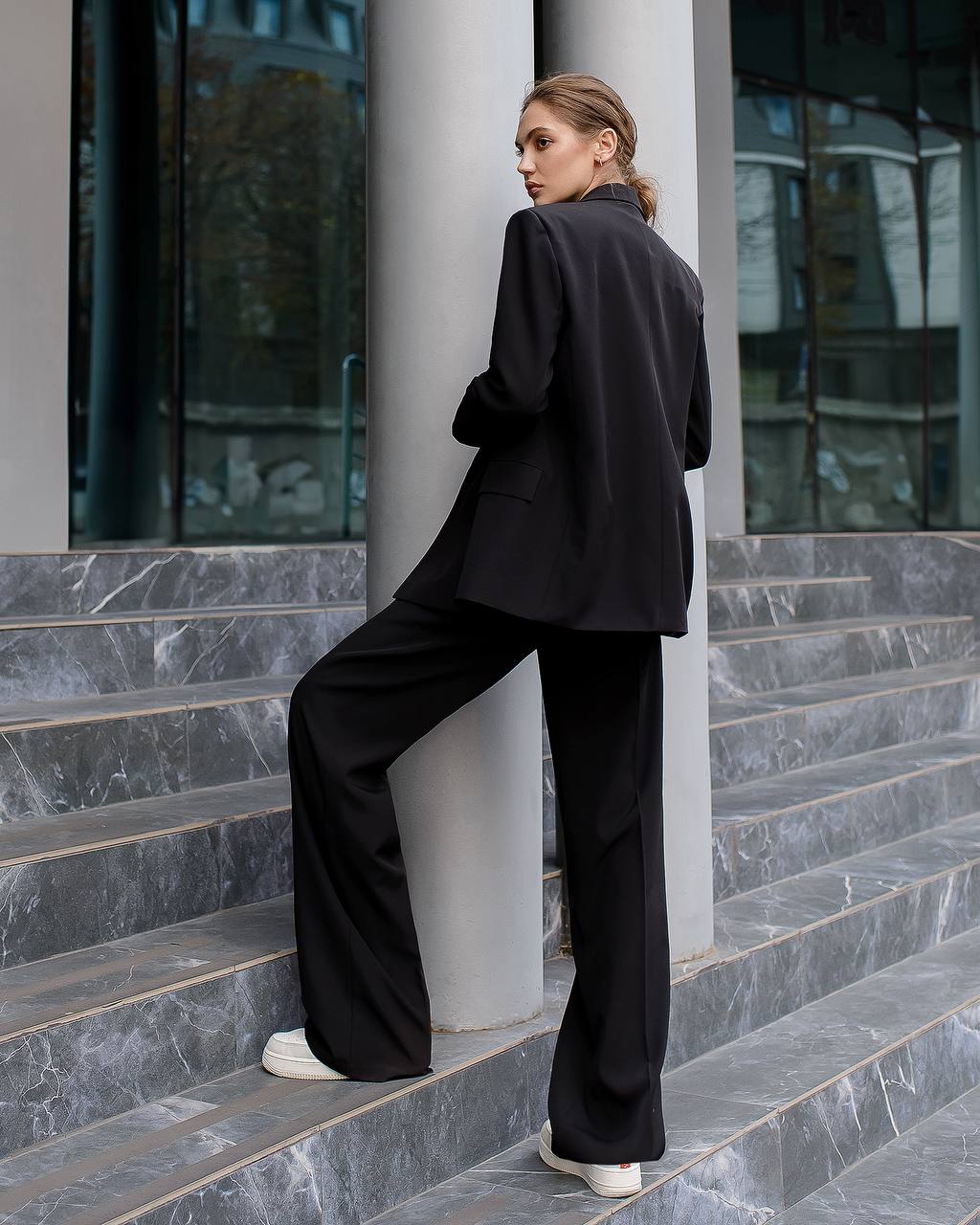Person wearing a black suit standing on steps with a modern building in the background