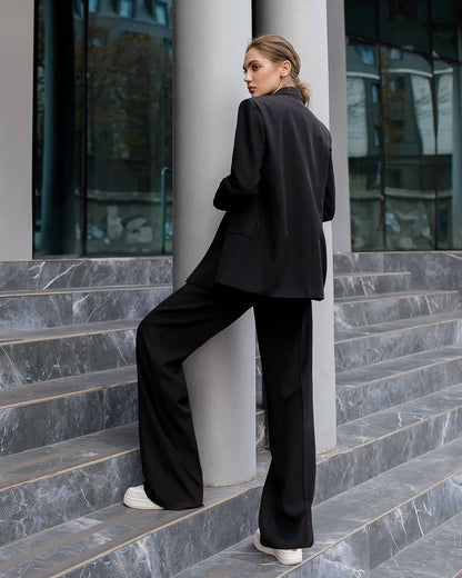 Person wearing a black suit standing on steps with a modern building in the background