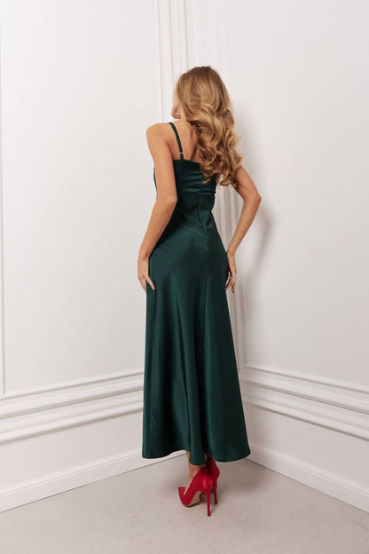 Woman in a long dark green dress with red high heels standing against a white wall.