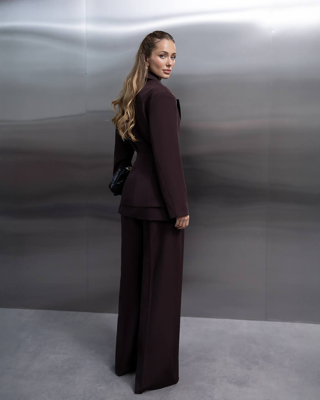 Woman in a dark brown suit standing against a plain background