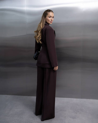 Woman in a dark brown suit standing against a plain background
