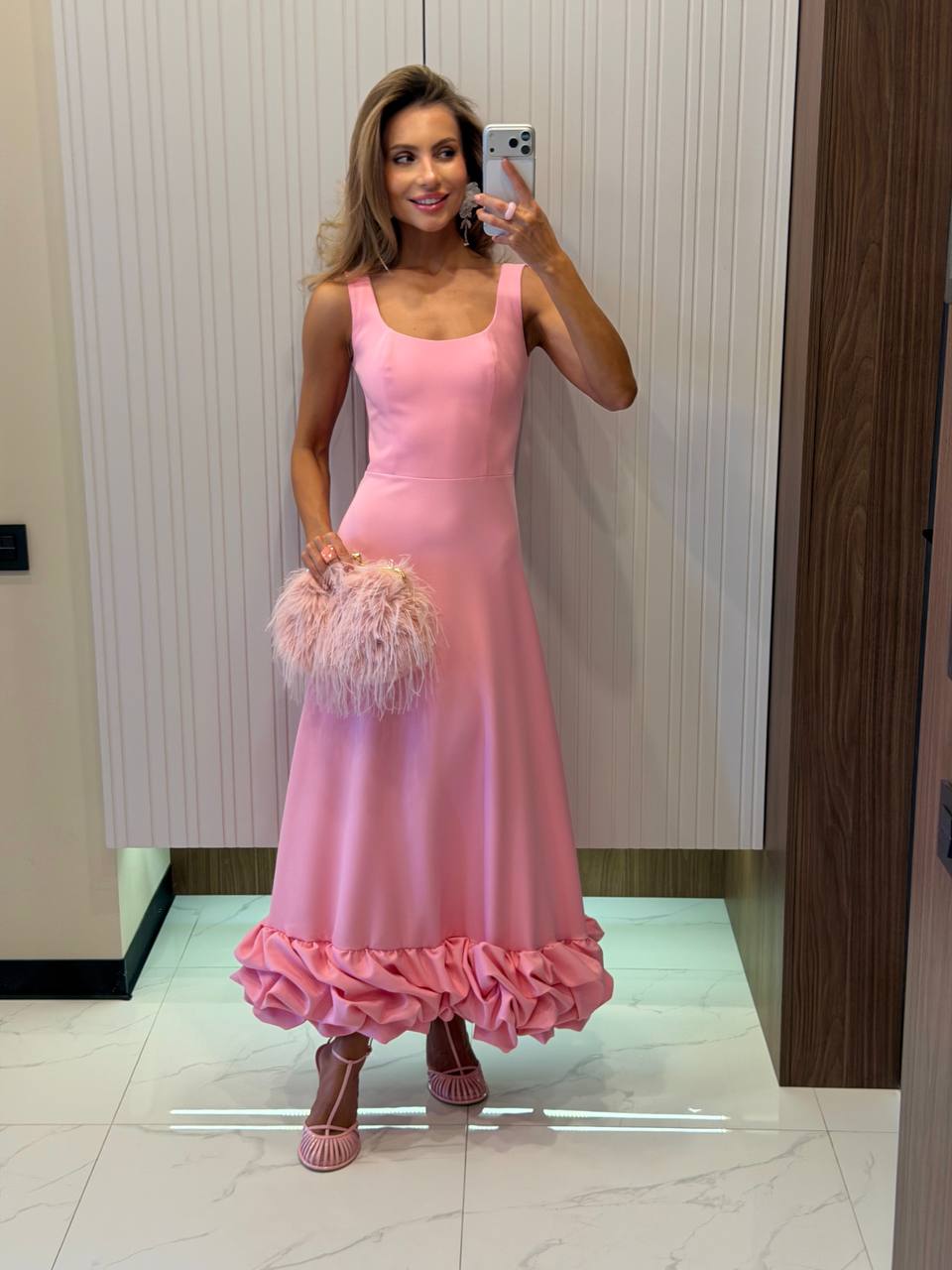 Woman in a pink dress taking a mirror selfie in an indoor setting.