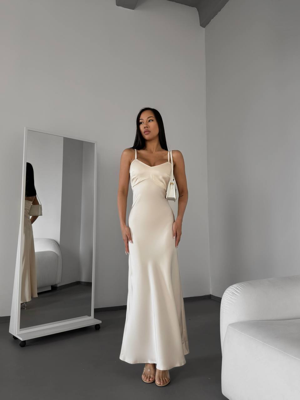 Woman in a white dress standing in a minimalistic room with a mirror.