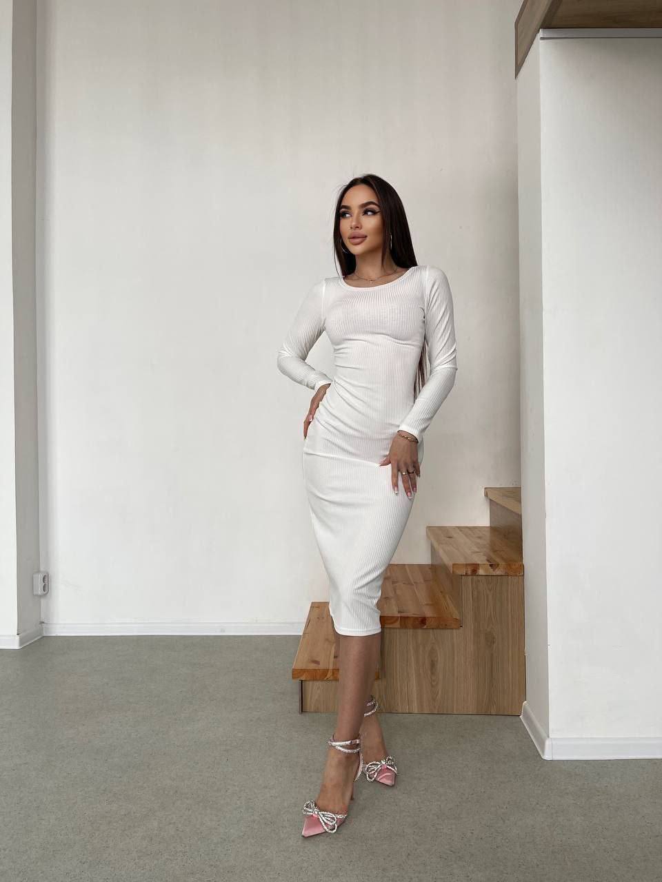 Woman in a white dress standing in a minimalistic room with a wooden bench.