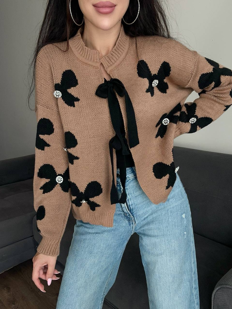 Person wearing a brown sweater with black bow designs and light blue jeans.