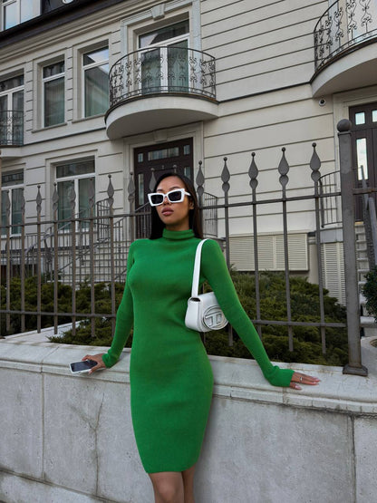 Woman in a green dress standing in front of a building with a white bag.