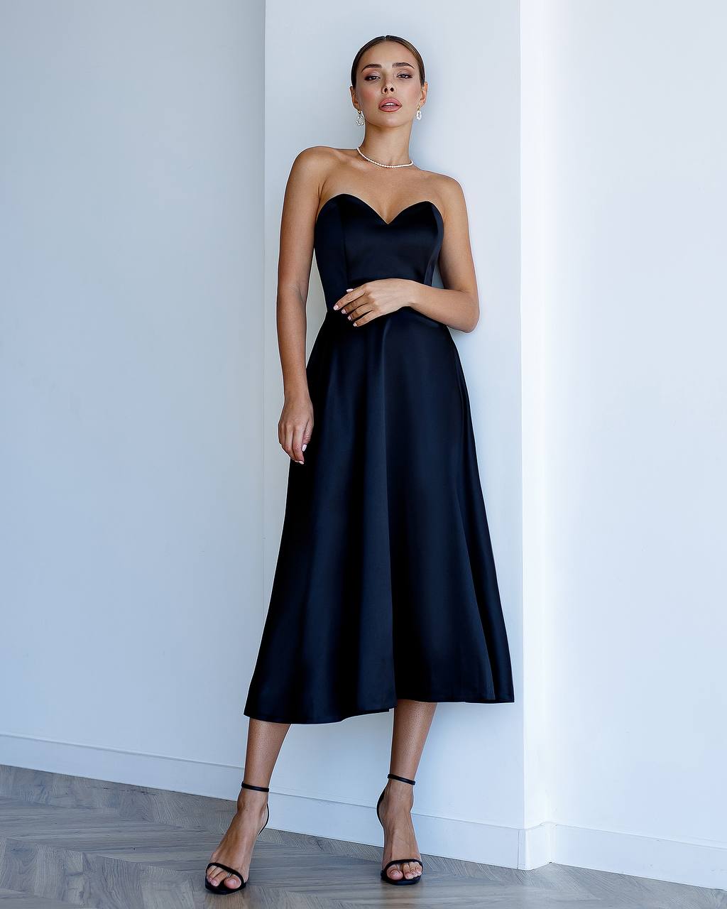 Woman wearing a black strapless dress against a white wall