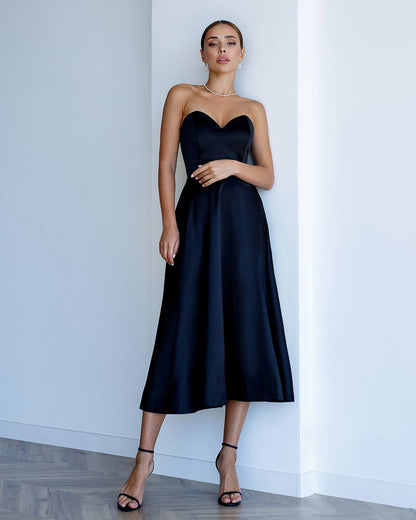 Woman wearing a black strapless dress against a white wall