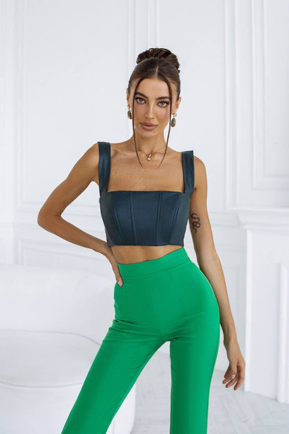 Woman wearing a black top and green pants against a white background