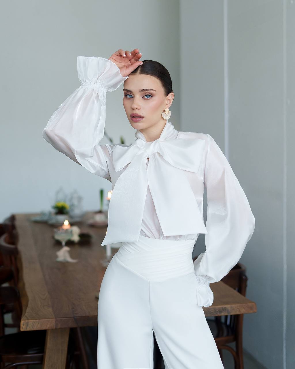 Woman in a white outfit posing in a room with a table and decor.