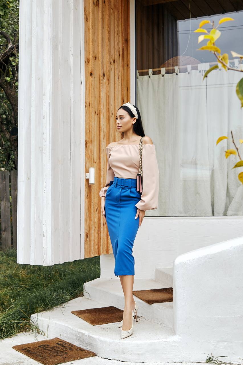 Woman in a beige top and blue pants standing on a white porch.