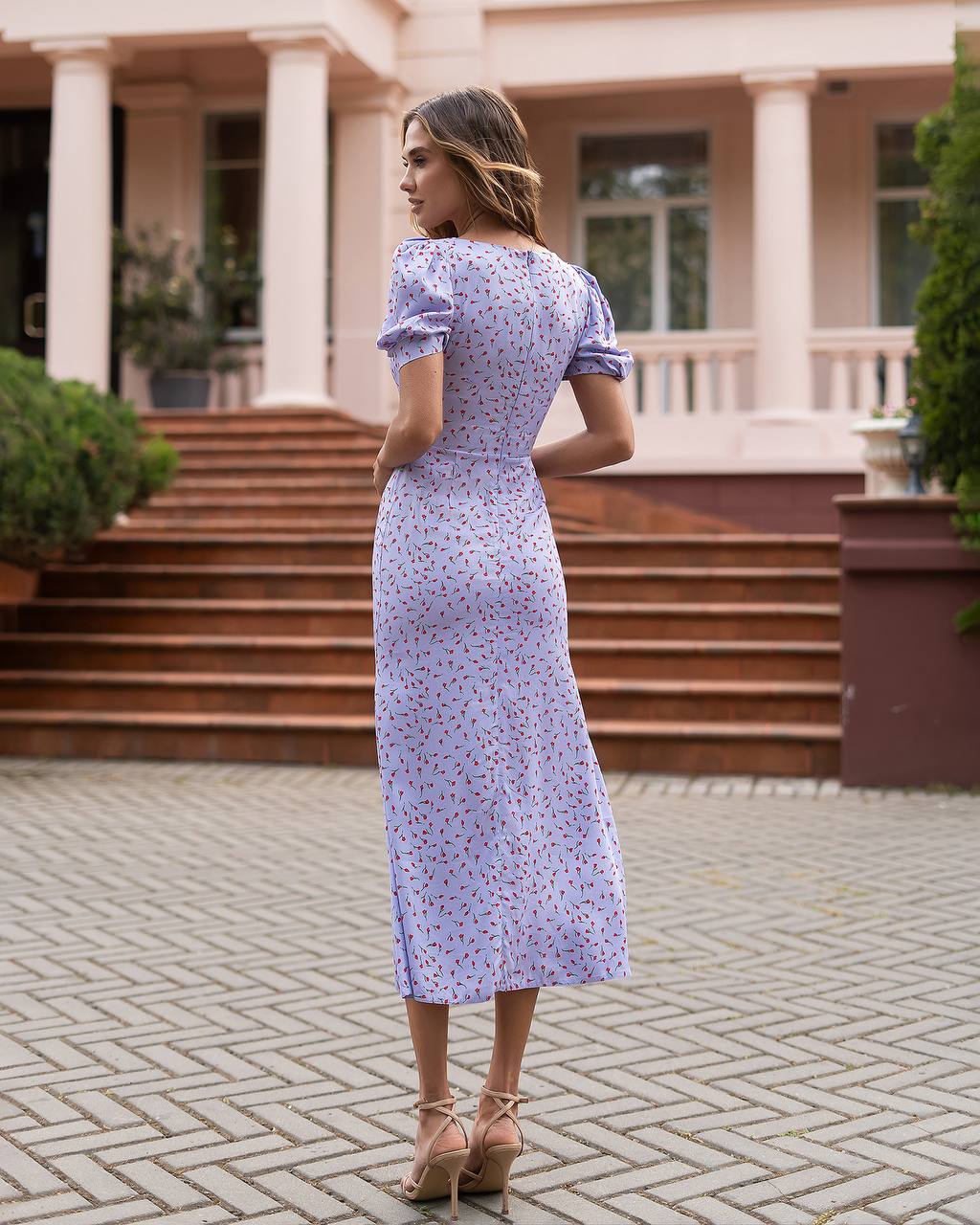 Woman in a floral dress standing in front of a large building with columns.