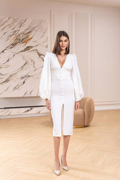 Woman in a white dress standing in a stylish room with marble wall and beige furniture.