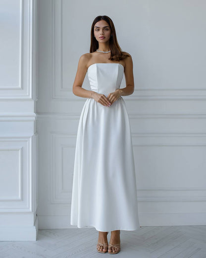 Woman wearing a white strapless dress standing against a white wall.