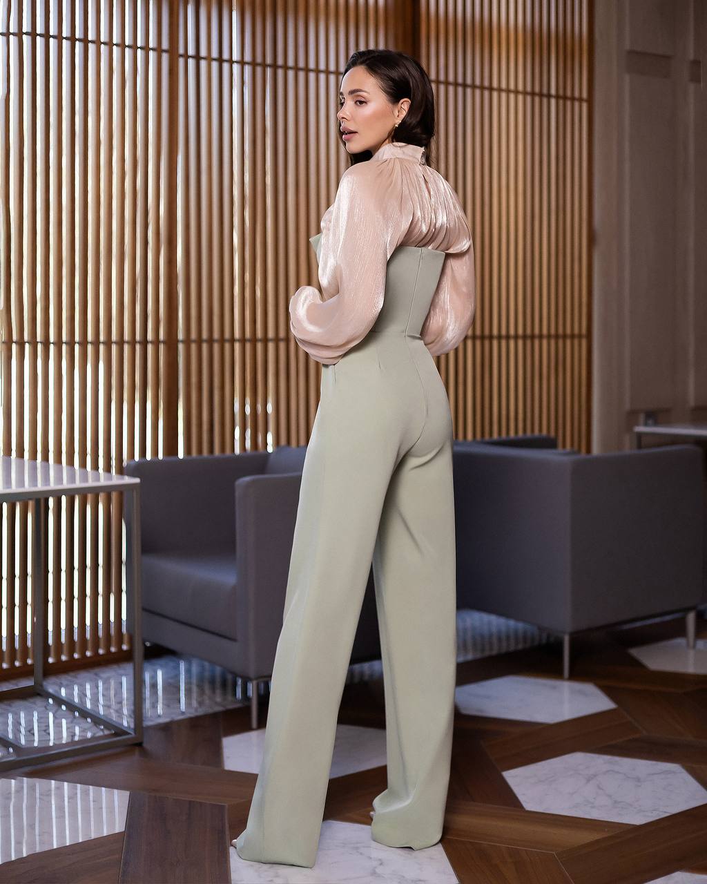 Woman in a stylish outfit standing in an elegant room with wooden paneling.