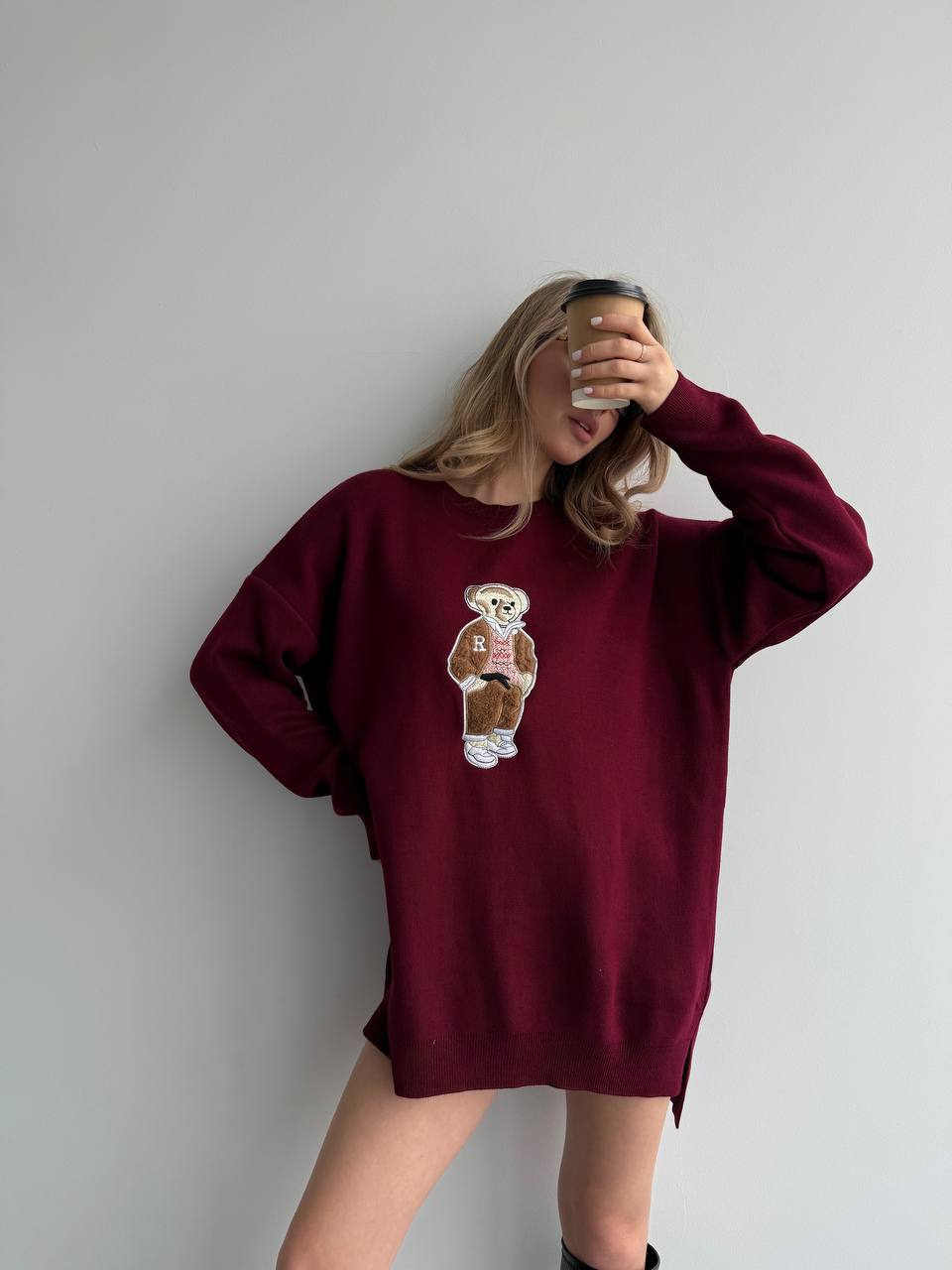 Person wearing a burgundy sweatshirt with a teddy bear graphic against a plain background