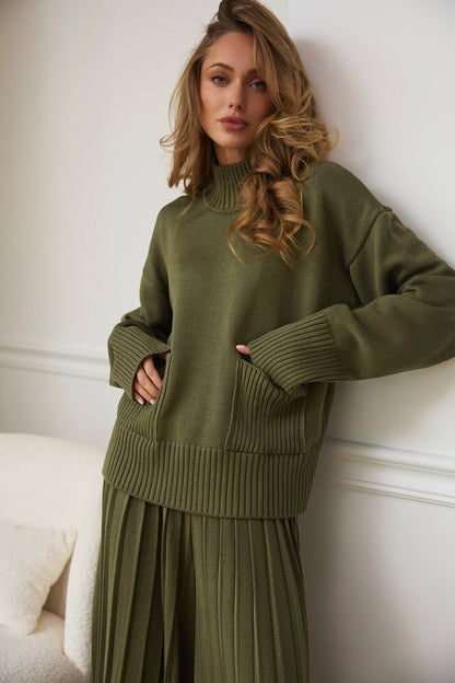 Woman wearing a green knit outfit against a white wall
