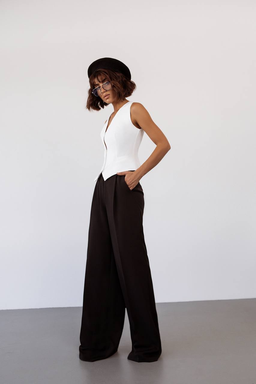 Woman wearing a white sleeveless top and black wide-leg pants against a white background