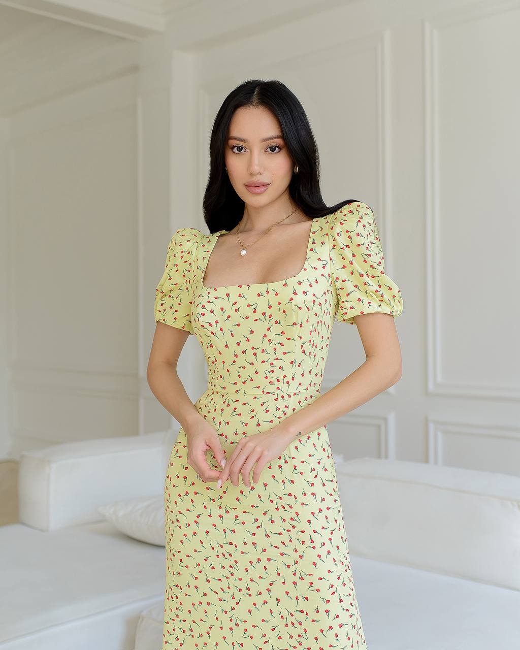 Woman wearing a yellow floral dress in a minimalistic room.