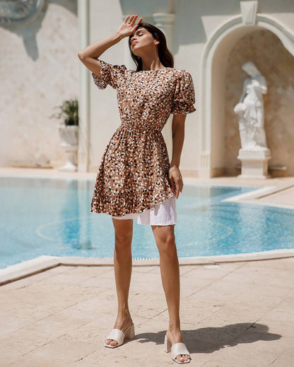 Woman in a floral dress standing by a pool with classical architecture in the background