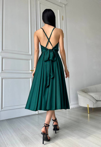 Woman wearing a green dress with a bow detail in a minimalistic room.