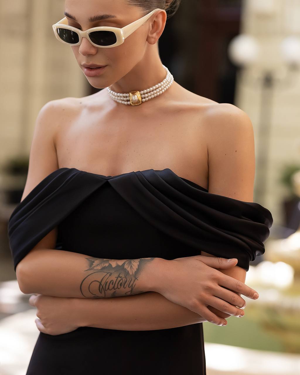 Woman wearing a black off-shoulder top with sunglasses and a pearl necklace.