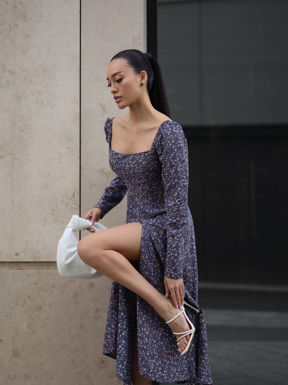 Woman in a floral dress standing against a wall