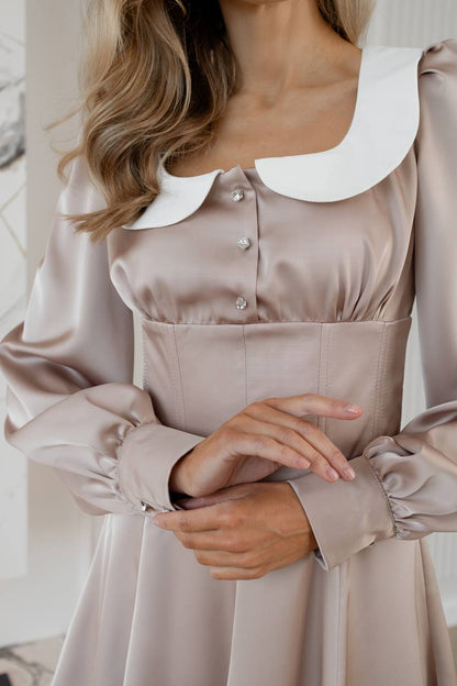 Close-up of a beige satin dress with a white collar and buttons.
