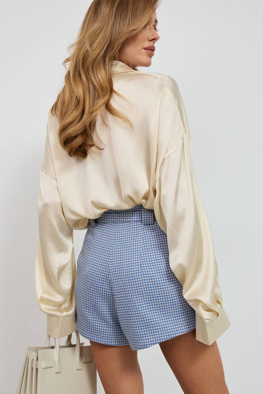 Woman wearing a beige blouse and blue checkered shorts against a white background