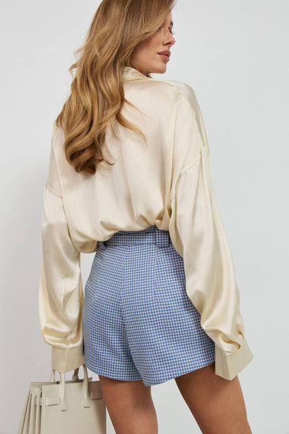 Woman wearing a beige blouse and blue checkered shorts against a white background