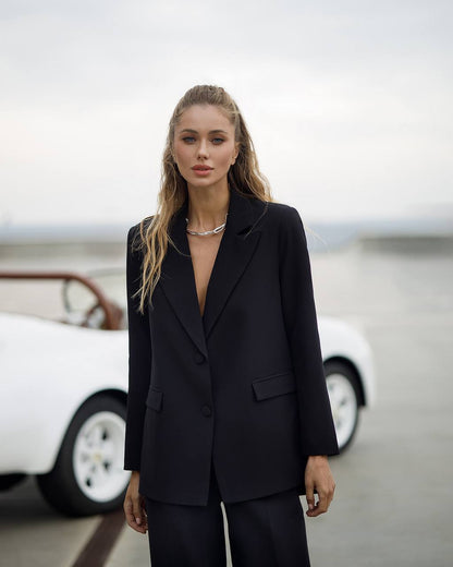 Woman in a black suit standing in front of a vintage car with a blurred background