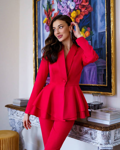 Woman in a red suit standing in a room with decorative elements and a colorful painting.