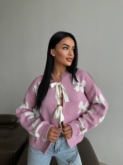 Woman wearing a pink sweater with white patterns against a plain background