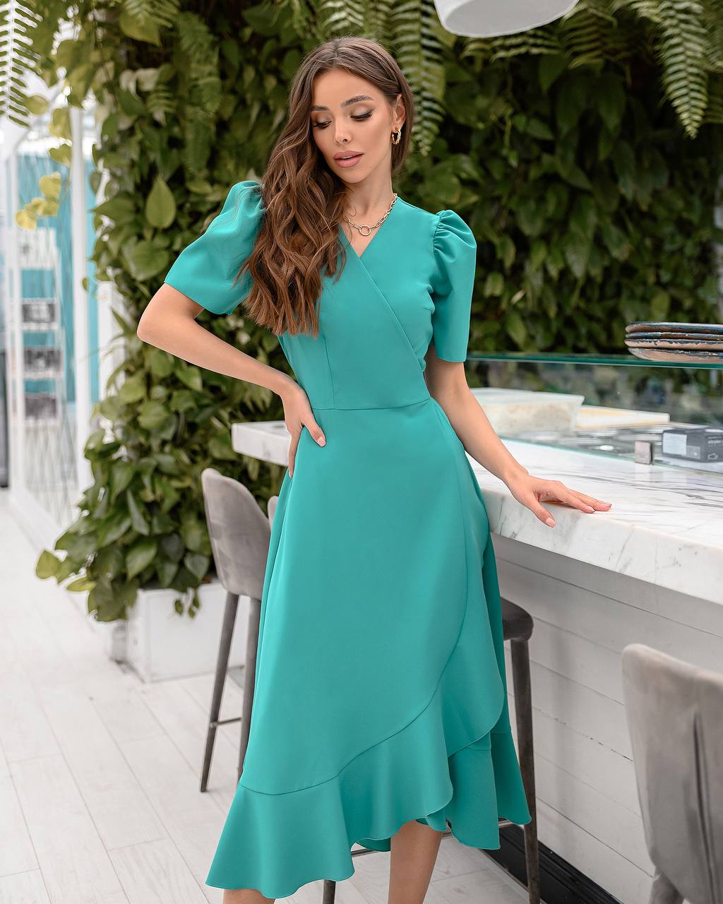 Woman in a teal dress standing in an outdoor setting with greenery.