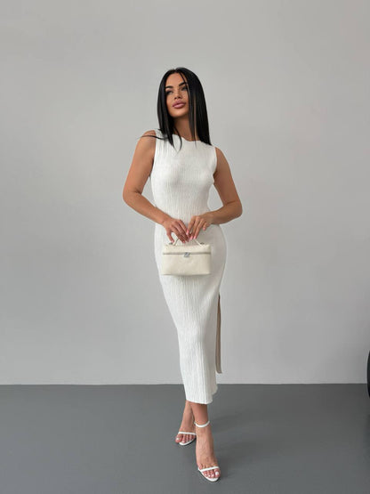 Woman in a white sleeveless dress holding a matching handbag against a gray background