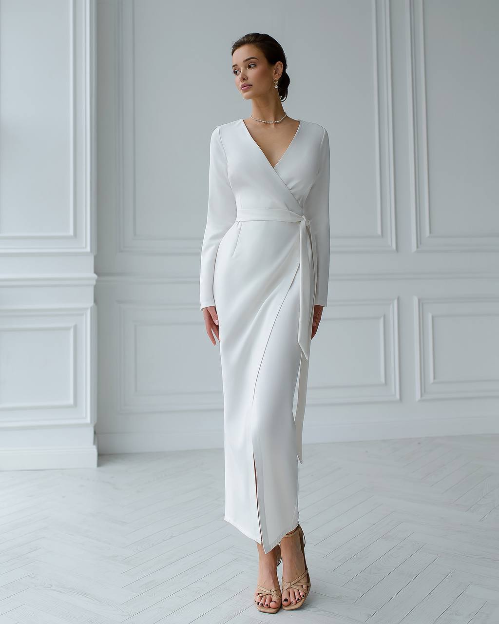 Woman wearing a white long-sleeve dress in a minimalistic room.