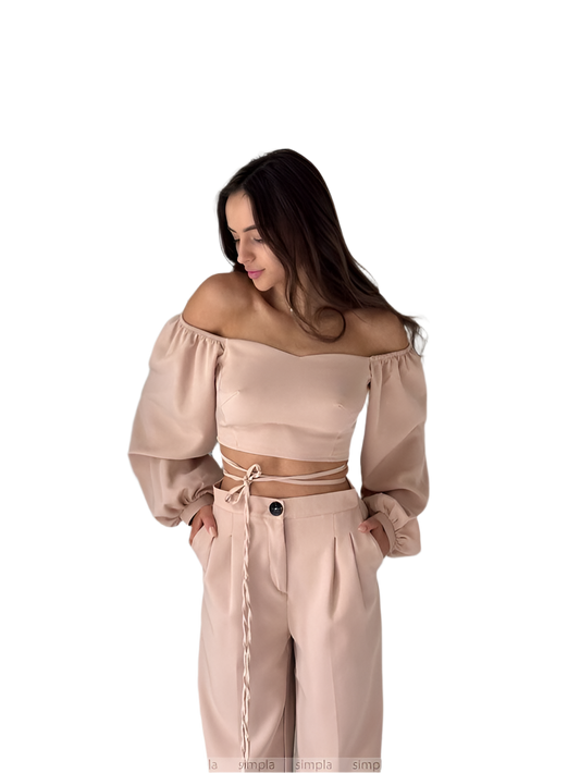 Woman wearing a beige off-shoulder top and high-waisted pants on a white background