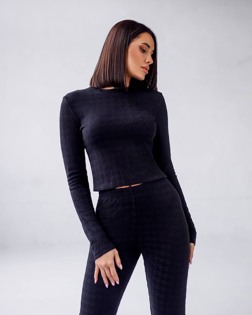 Woman wearing a black long-sleeve top and leggings against a white background